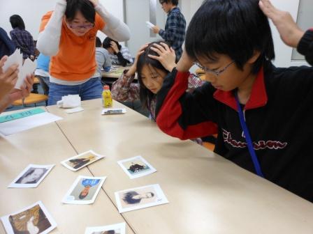 手を頭に置いてかるたをする子供と先生