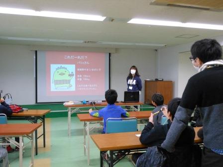 スクリーンの横に立って話す先生 スクリーンの横に立って話す先生